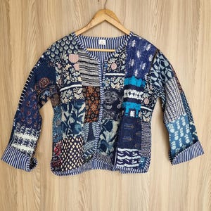 Könnte beinhalten: Eine blaue und weiße Patchwork-Steppjacke mit Knopfleiste. Die Jacke hat verschiedene florale und geometrische Muster.