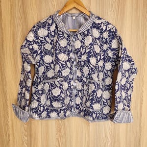 Könnte beinhalten: Eine gesteppte Jacke mit blauem und weißem Blumenmuster, Knopfleiste und langen Ärmeln. Die Jacke hat einen gestreiften Kragen und Ärmelbündchen.