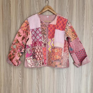 Könnte beinhalten: Eine rosafarbene und rote Patchwork-Steppjacke mit Knopfleiste. Die Jacke hat einen Blumendruck und ist aus Baumwolle.
