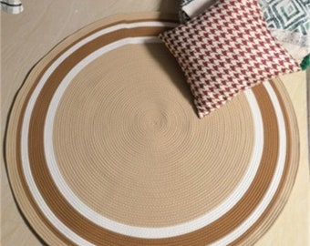 May include: A round, beige, woven rug with white and brown stripes. The rug has a circular design with a center circle and concentric circles radiating outwards.