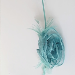 May include: A light blue fabric flower with a stem and feathers. The flower is made of a delicate, mesh-like material and has a soft, romantic look.