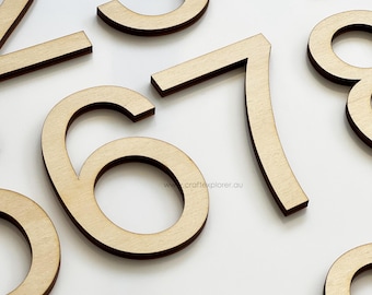 May include: A collection of laser-cut wooden numbers featuring a light tan natural wood grain finish. The digits 2, 3, 4, 6, 7, 8, and 9 are visible, each displaying a clean sans-serif typeface. The text www.craftexplorer.au is printed on the number 6.