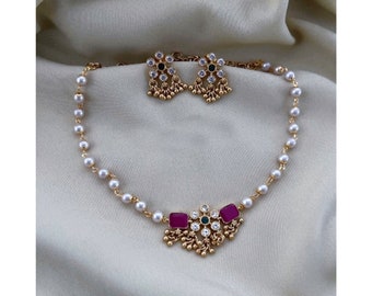 May include: A gold necklace with a pearl chain and a pendant featuring pink and green stones. Matching earrings with a similar design are included.