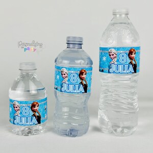 Peut inclure: Trois bouteilles d'eau en plastique transparent de tailles diff&eacute;rentes, chacune avec une &eacute;tiquette bleue &agrave; bordure scintillante, des flocons de neige et deux personnages de dessin anim&eacute;. Le num&eacute;ro 8 et le nom JULIA sont inscrits.