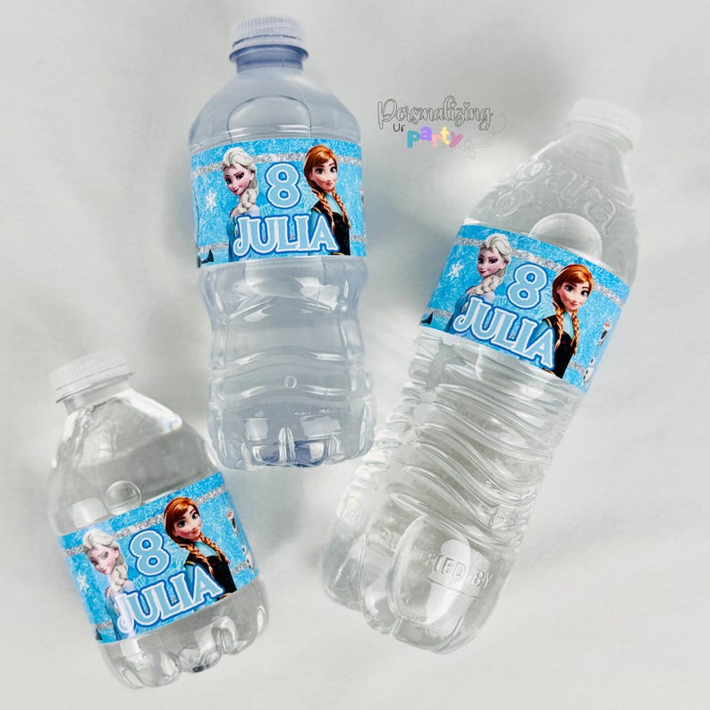 Peut inclure: Trois bouteilles d'eau en plastique transparent avec des &eacute;tiquettes bleues personnalis&eacute;es repr&eacute;sentant les personnages Elsa et Anna, le chiffre 8 et le nom JULIA en blanc. Les &eacute;tiquettes ont une bordure bleue scintillante et des flocons.