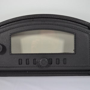 May include: Black cast iron pizza oven door with a glass window and a round knob. The door has a curved top and a rectangular frame.