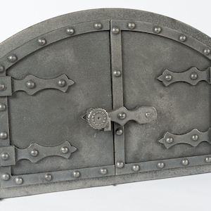 Könnte beinhalten: Ein Paar gewölbte Metaltüren mit einem Riegel und Scharnieren. Die Türen sind aus dunkelgrauem Metall und haben ein rustikales, antikes Aussehen.
