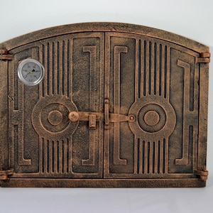 Puede incluir: Una puerta de chimenea de hierro fundido de doble hoja con un diseño decorativo y un termómetro incorporado. La puerta es de color marrón oscuro con un acabado de cobre.