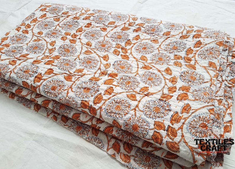 Puede incluir: Una pila de tela de algod&oacute;n blanca con un estampado floral en tonos naranja y azul. La tela est&aacute; doblada en tres partes y tiene una etiqueta "TEXTILES CRAFT" en la esquina inferior derecha.
