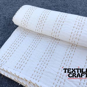 May include: White fabric with brown stitching in a striped pattern. The fabric is folded in half and the text "TEXTILES + CRAFT" is visible in the bottom right corner.