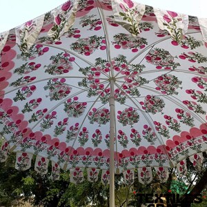 May include: A white umbrella with a floral pattern in pink and green. The umbrella has a scalloped edge with pink trim and decorative hanging fabric. The umbrella is open, showing the interior design.