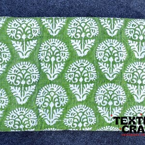 May include: Green kantha quilt with a white floral pattern. The quilt is made of cotton and is hand-stitched. The quilt is folded and laid flat on a gray surface. The text "TEXTILES CRAFT" is visible in the lower right corner of the image.
