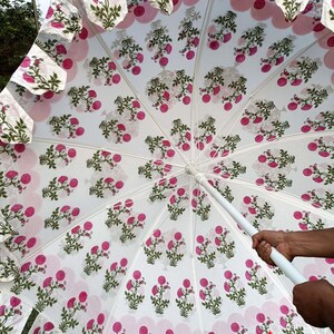 May include: A white umbrella with a floral pattern in pink and green. The umbrella has a scalloped edge and is held by a white handle. The text "TEXTILES CRAFT" is visible.