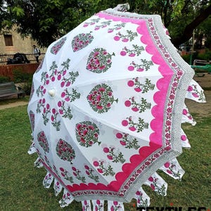 May include: A white parasol with a floral pattern in pink and green. The parasol has a scalloped pink border and a decorative fringe. The text "TEXTILES CRAFT" is visible at the bottom right.