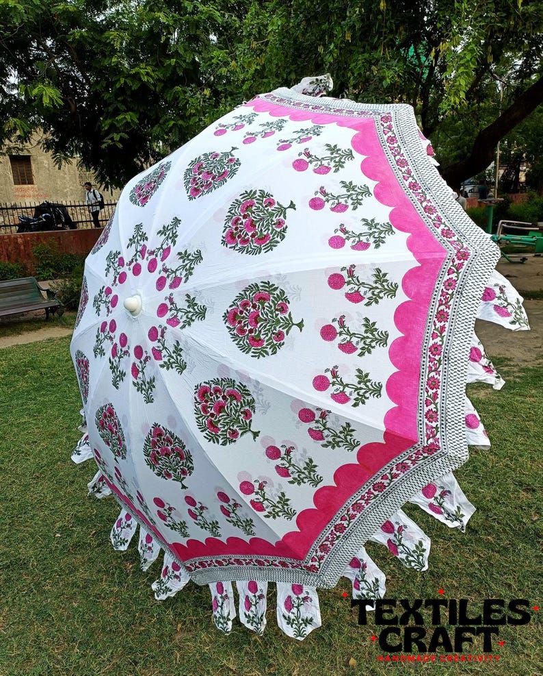 May include: A white parasol with a floral pattern in pink and green. The parasol has a scalloped pink border and a decorative fringe. The text "TEXTILES CRAFT" is visible at the bottom right.