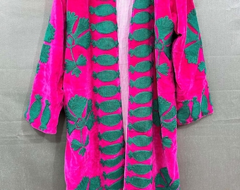 May include: A vibrant pink velvet coat with green embroidered leaf and oval designs. The coat has long sleeves and a striped lining. The text "TEXTILES CRAFT" is visible on the lower right.