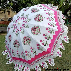 May include: White and pink floral print umbrella with a scalloped edge. The umbrella features a repeating pattern of pink flowers and green leaves on a white background. The border is a solid pink with a decorative edge.