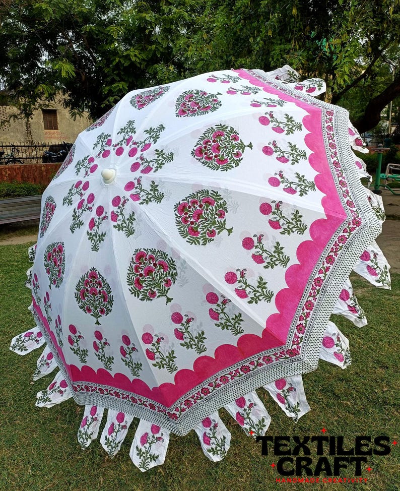 May include: White and pink floral print umbrella with a scalloped edge. The umbrella features a repeating pattern of pink flowers and green leaves on a white background. The border is a solid pink with a decorative edge.