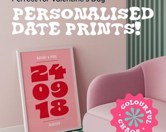 Op de afbeelding: Gepersonaliseerde datumafdruk met een wit frame en roze achtergrond. De afdruk heeft een rode datum in een vetgedrukt lettertype, met de tekst "Rachel & Paul" en "Forever" in wit. De afdruk is op een geruit groen en wit oppervlak.