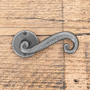 Pode incluir: Uma maçaneta de porta de metal cinza-escuro com um design curvo em forma de S e uma placa de montagem circular. A maçaneta apresenta um acabamento fosco texturizado e é fixada à superfície com dois parafusos Phillips visíveis na base.