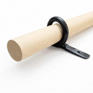 May include: A light-colored wooden rod with a black metal ring and bracket. The rod is round and appears to be unfinished. The black metal ring is attached to the rod with a bracket, suggesting a curtain rod or similar item.