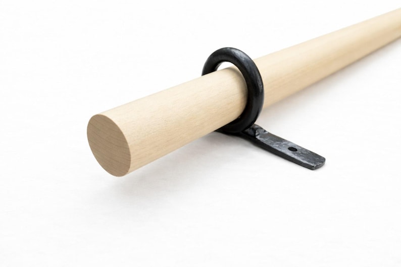 May include: A light-colored wooden rod with a black metal ring and bracket. The rod is round and appears to be unfinished. The black metal ring is attached to the rod with a bracket, suggesting a curtain rod or similar item.