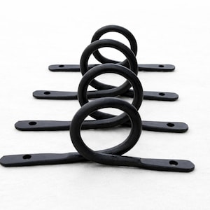 May include: Black metal hardware with a looped design. Each piece has a circular loop connected to a flat, rectangular base with a hole at each end. The hardware is arranged in a row against a white background.