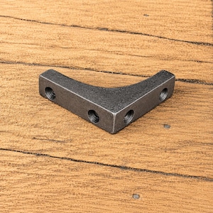 Può includere: Una staffa angolare in metallo grigio scuro con design a forma di L. La staffa presenta una finitura opaca e liscia e include quattro fori circolari preforati per il montaggio, con due fori posizionati su ciascun lato della struttura.