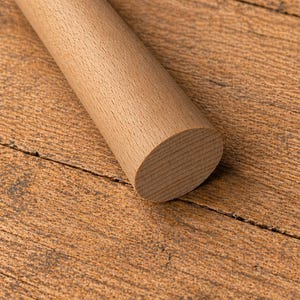 May include: A light brown, cylindrical wooden rolling pin with a rounded end, resting on a textured, brown wooden surface. The rolling pin is made of solid wood and has a smooth, natural finish. The wood grain is visible.