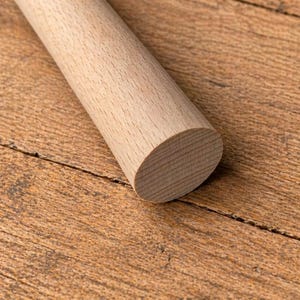 May include: A wooden rolling pin with a rounded end, resting on a wooden surface. The rolling pin is light brown and cylindrical, with visible wood grain. The background is a textured, warm-toned wooden surface.