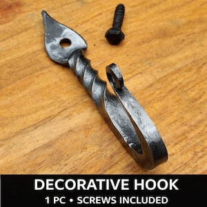 Könnte beinhalten: Ein dekorativer, handgeschmiedeter Metallhaken mit einem gedrehten Design und einer blattförmigen Spitze. Inklusive einer schwarzen Schraube zur Montage. Der Haken wird auf einer Holzoberfläche gezeigt. Der Text auf dem Bild lautet "DECORATIVE HOOK".
