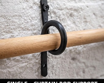 May include: A black, single curtain rod support mounted on a white brick wall. The support features a circular ring and a vertical bracket, holding a wooden rod. The text at the bottom reads "SINGLE • CURTAIN ROD SUPPORT".