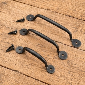 Peut inclure: Trois poignées de meubles en métal noir avec des vis assorties sur une surface en bois. Chaque poignée a une barre incurvée et des plaques de montage circulaires. Les vis sont noires et ont une pointe.