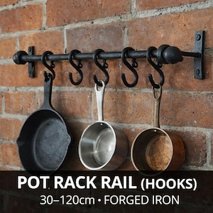 Op de afbeelding: Zwarte smeedijzeren pottenrek met haken, gemonteerd op een bakstenen muur. Drie potten hangen aan de haken. Het pottenrek is 30-120 cm lang.