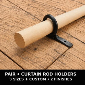 Könnte beinhalten: Ein schwarzer Gardinenstangenhalter aus Metall mit einer kreisförmigen Ringhalterung an einer flachen Montageplatte, der eine helle Holzstange trägt. Der Text unten lautet: PAIR • CURTAIN ROD HOLDERS 3 SIZES + CUSTOM • 2 FINISHES.