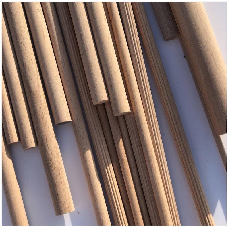 May include: A collection of unfinished wooden dowels and decorative molding pieces. The dowels are cylindrical and vary in diameter. Some molding pieces have a grooved design. The wood has a light brown color and a natural grain.