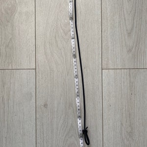 May include: A black bungee cord with a loop at each end, measured with a white tape measure that shows numbers 1 through 52.