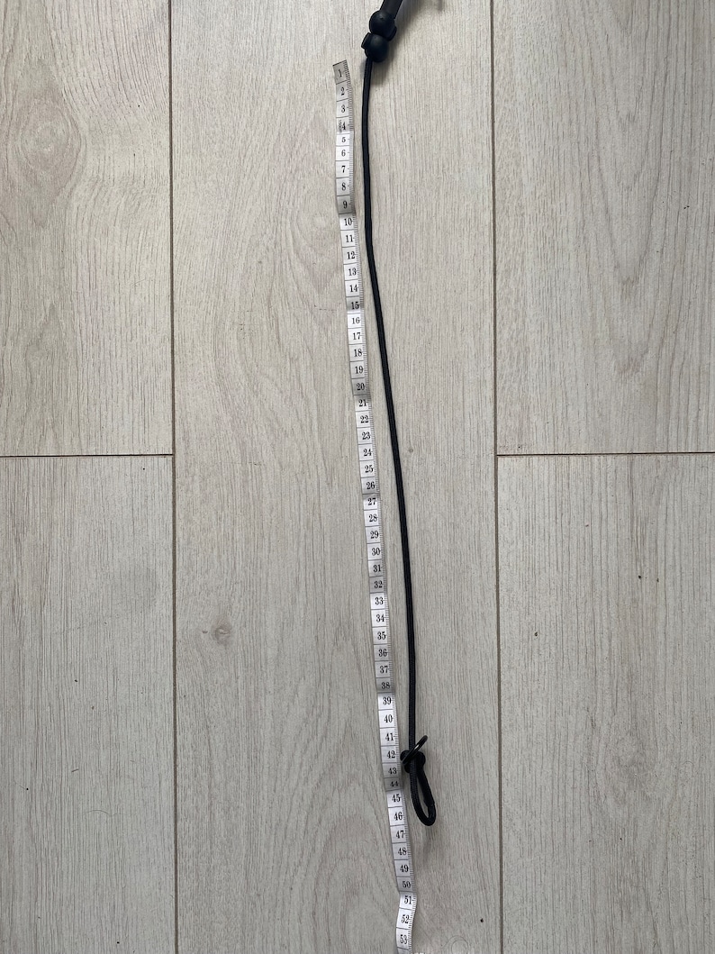 May include: A black bungee cord with a loop at each end, measured with a white tape measure that shows numbers 1 through 52.