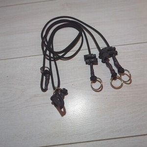 May include: Three black cords with silver rings and black plastic clips at the ends. The cords are looped together.