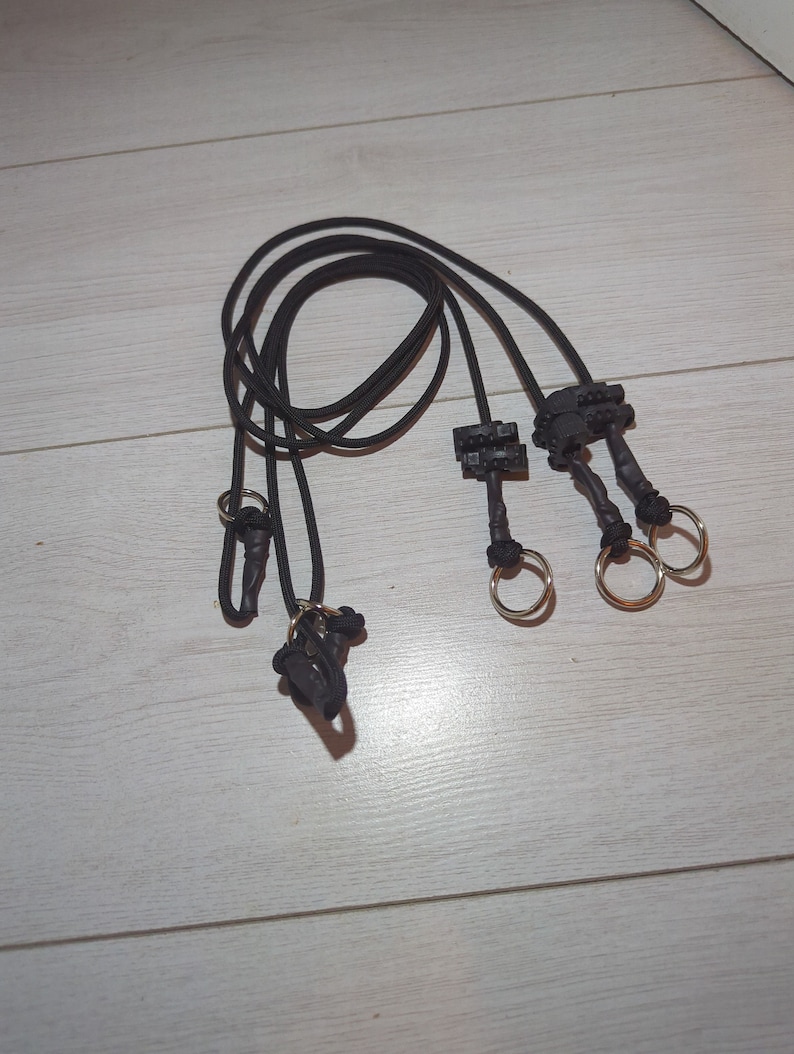 May include: Three black cords with silver rings and black plastic clips at the ends. The cords are looped together.