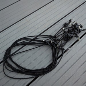 May include: A bundle of black elastic cord with silver metal clasps. The cord is coiled in a circle and the clasps are visible at the top of the coil.