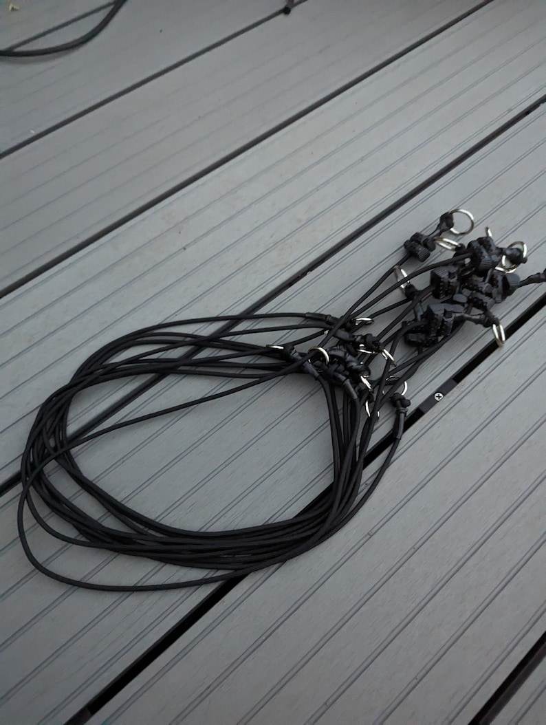 May include: A bundle of black elastic cord with silver metal clasps. The cord is coiled in a circle and the clasps are visible at the top of the coil.