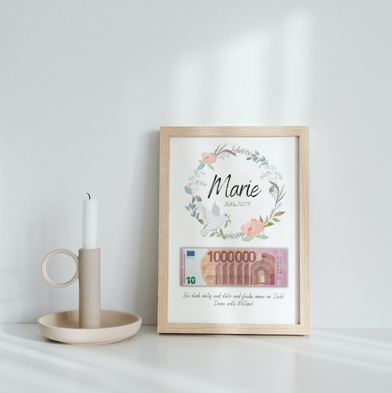 May include: A framed print with a watercolor wreath of flowers and a dove. The wreath surrounds the name "Marie" and the date "16.04.2023". A 10 euro bill is tucked inside the frame. The text below the wreath reads "Sex dank, messy and stols and glade wour on Dech! Dear ante illan!"