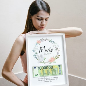 May include: A white framed print with a floral wreath and a dove. The print has a fake 100 euro bill with the number 1,000,000 printed on it. The text on the print reads "Marie 16. Mai 2023 Herzlichen Gl&uuml;ckwunsch zur Kommunion und zur ersten Million w&uuml;nschen Dir Mama und Papa."