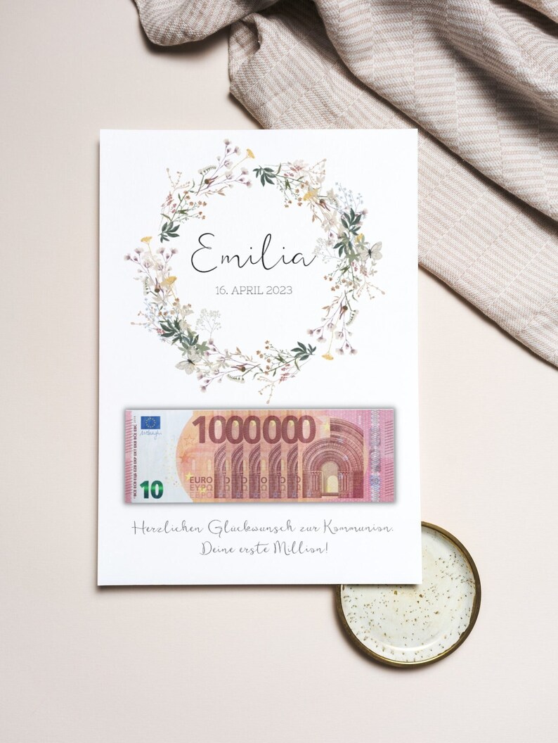 May include: A white card with a floral wreath and the text "Emilia 16. APRIL 2023". A fake 10 euro bill with the number 1,000,000 printed on it is attached to the card. The text "Herzlichen Gl&uuml;ckwunsch zur Kommunion Deine erste Million!" is printed below the bill.