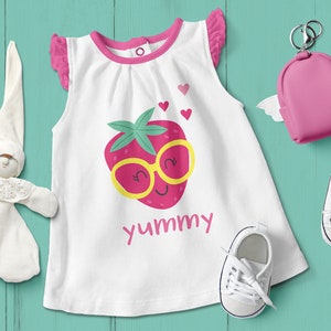 May include: White sleeveless baby onesie with pink trim and a strawberry graphic. The strawberry has a yellow face with sunglasses and the text "yummy" is printed below.
