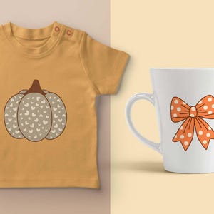 May include: Mustard yellow baby tee with a pumpkin graphic. The pumpkin is gray with white heart details and a brown stem. A white mug with an orange bow with white polka dots is also shown.