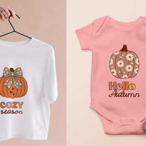 May include: A white t-shirt with an orange pumpkin design and the words "COZY season". A pink baby onesie with a pumpkin design and the words "Hello Autumn". Orange and white baby shoes are next to the onesie.