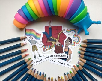 May include: A set of 20 blue colored pencils arranged in a semi-circle around three stickers. The stickers feature illustrations of people and the text "Can't be straight... Sit straight. Can't think straight." A rainbow-colored plastic toy in the shape of a caterpillar is above the pencils and stickers.