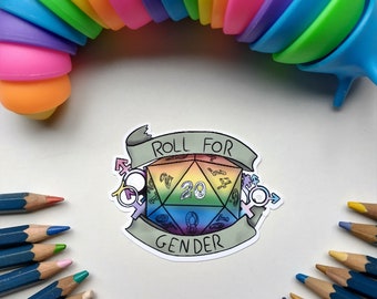 May include: A rainbow-colored silicone toy in the shape of a horseshoe is above a sticker of a twenty-sided die with the words "Roll for Gender" on a white background.  There are a circle of blue pencils around the sticker.
